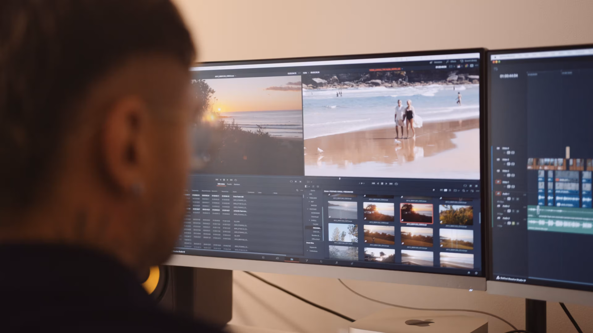 A person sits at a desk editing videos on a widescreen monitor. The screen displays video production Sydney software with beach and sunset clips, file thumbnails, and a timeline. The modern workspace includes another partially visible monitor.