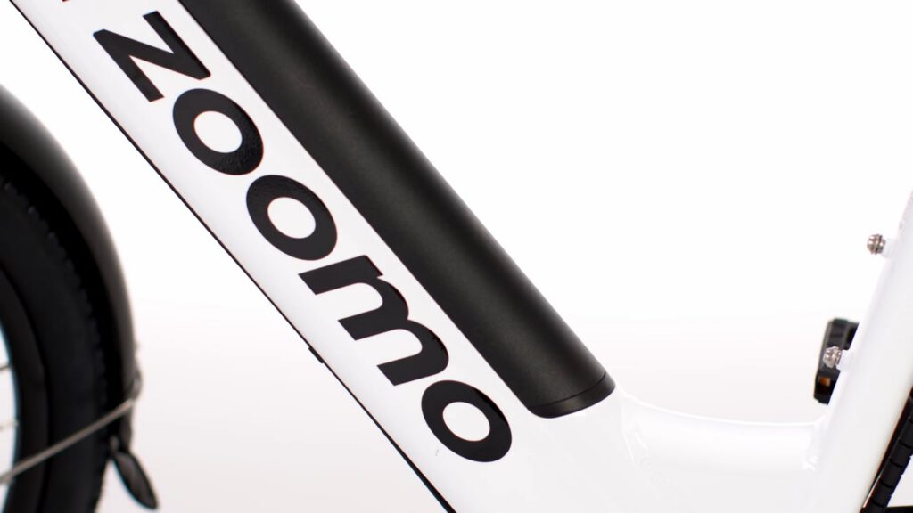 Close-up of a white bicycle frame featuring the bold, black text “Zoomo” printed vertically along a black diagonal tube. The background is plain white, emphasising the bike’s branding and sleek, modern design. Only part of the bike is visible.